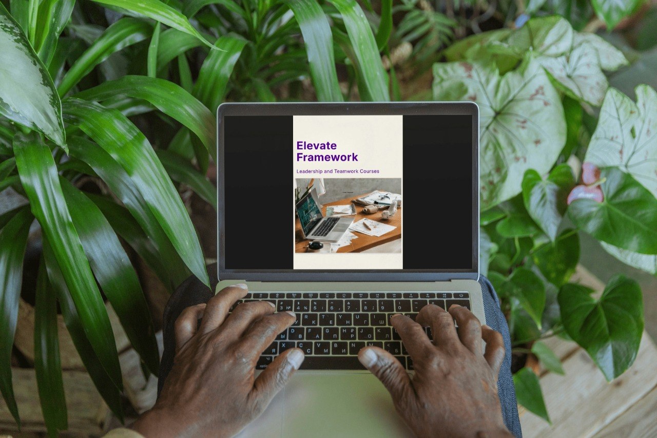Person using a laptop with 'Elevate Framework' displayed on the screen, surrounded by green plants.